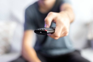 A man sitting on a sofa changes the channel with a remote control. selective focus clipart