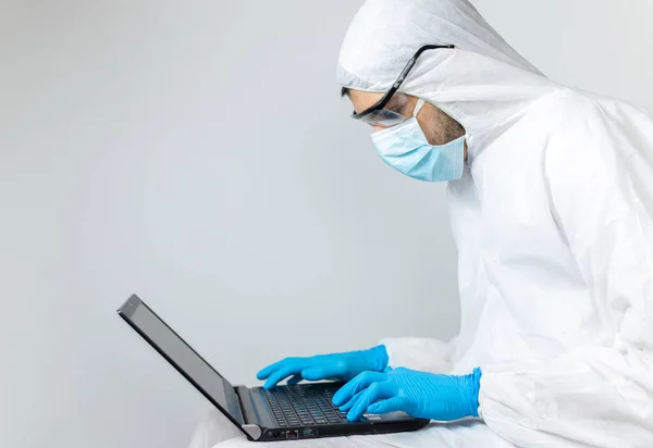 Bilgisayarıyla çalışan araştırmacı covid-19 Coronavirus koruyucu giysiler giyiyor.