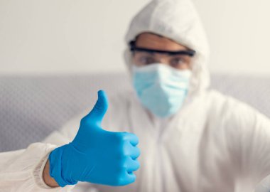 Evde koronavirüs için karantinaya alınmış mavi lateks eldivenler ve koruyucu giysiler giymiş bir adam.