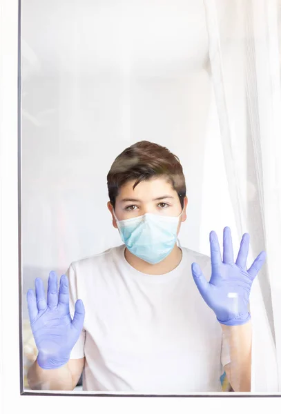 在验尸官检疫期间 戴着防护面具和蓝色手套的男孩从窗户向外张望 — 图库照片