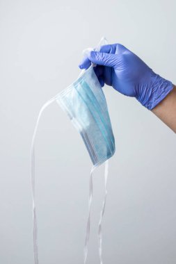 Mavi eldivenli el, bir koronavirüs maskesini atıyor. Koronavirüs salgınının sonu kavramı.