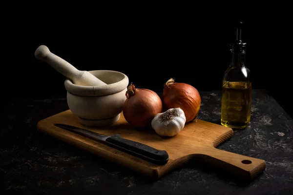 cooking scene with mortar, garlic, onions, knife and cutting board. Dark food style