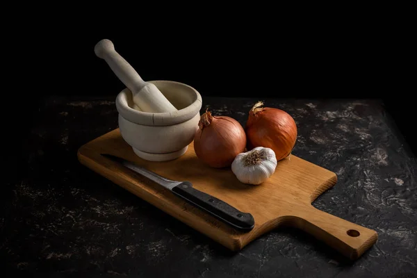 cooking scene with mortar, garlic, onions, knife and cutting board. Dark food style