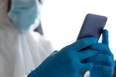 Coperid-19 için koruyucu giysileri olan doktor ameliyathanede cep telefonunu izliyor.