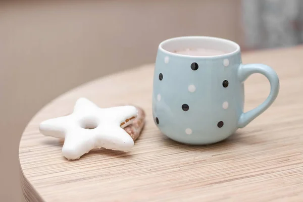 a light blue mug with black and white dots and a white star shaped cookie on a beige wooden table