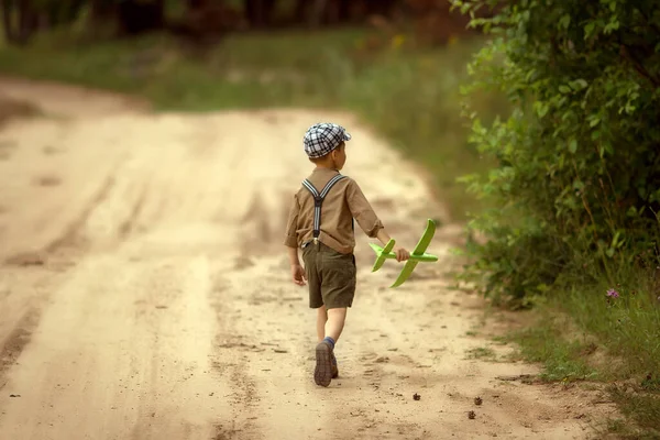 boy in shorts with suspenders, a shirt and a cap is playing in the woods with a toy airplane. Retro style and concept of military themes.