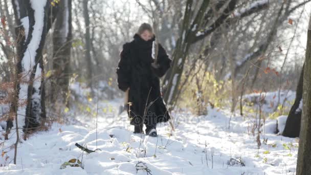 Un adolescente con un abrigo de piel sacando leña del bosque. Niño siberiano con un hacha en el bosque. Un niño con un abrigo de piel en el invierno en el pueblo . — Vídeos de Stock