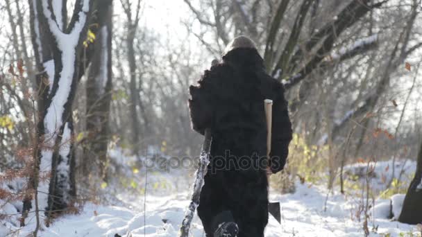 Un adolescente con una pelliccia che estrae legna dalla foresta. Ragazzo siberiano con un'ascia nella foresta. Un ragazzo in pelliccia in inverno nel villaggio . — Video Stock