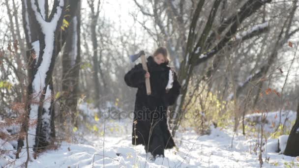 Un adolescente con un abrigo de piel sacando leña del bosque. Niño siberiano con un hacha en el bosque. Un niño con un abrigo de piel en el invierno en el pueblo . — Vídeos de Stock