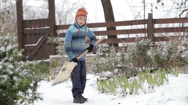 Boy removes snow shovel near the house. Cleaning snow in the winter near the house. The child cleans shovel the snow covered track. — Stock Video