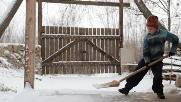 Rapaz remove pá de neve perto da casa. Limpeza de neve no inverno perto da casa. A criança limpa a pá a pista coberta de neve . — Vídeo de Stock