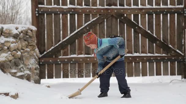 Garçon enlève la pelle à neige près de la maison. Nettoyage de la neige en hiver près de la maison. L'enfant nettoie la pelle sur la piste enneigée . — Video
