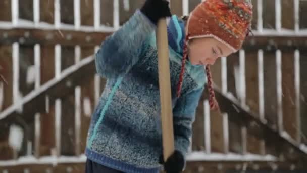 Boy removes snow shovel near the house. Cleaning snow in the winter near the house. The child cleans shovel the snow covered track. — Stock Video