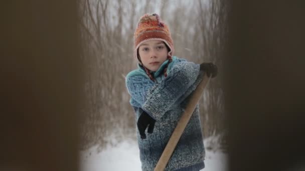 Il ragazzo pulisce la neve vicino alla recinzione. Il bambino pulisce l'inverno di traccia. Una vista attraverso una recinzione sulla neve pulizia adolescente . — Video Stock