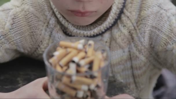 Drengen kigger på cigaretskod i en tallerken. En teenager ser på cigaretskod. Anti tobak video. For en sund livsstil . – Stock-video
