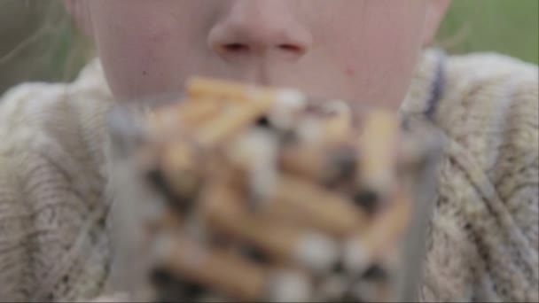 O rapaz está a olhar para pontas de cigarro num prato. Um adolescente olha para as pontas de cigarro. Vídeo anti-tabaco. Para um estilo de vida saudável . — Vídeo de Stock