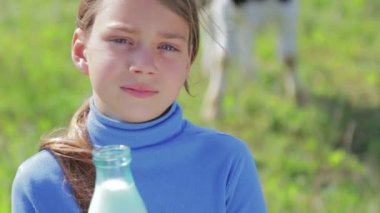 Bir çocuk portresi ile bir şişe süt bir çayırda. Bir çocuk bir alanda yakınındaki bir inek süt içiyor. Sağlıklı bir yaşam tarzı. Sağlıklı beslenme. 