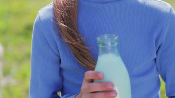 Portret van een jongen met een fles melk in een weiland. Een jongen drinkt melk in de buurt van een koe in een veld. Gezonde levensstijl. Gezond eten. — Stockvideo