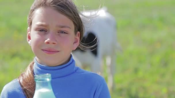 Ritratto di un ragazzo con una bottiglia di latte in un prato. Un ragazzo beve latte vicino a una mucca in un campo. Uno stile di vita sano. Note di alimentazione . — Video Stock