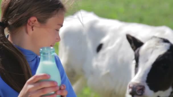 Porträtt av en pojke med en flaska mjölk på en äng. En pojke dricker mjölk nära en ko i ett fält. Hälsosam livsstil. Sunda matvanor. — Stockvideo