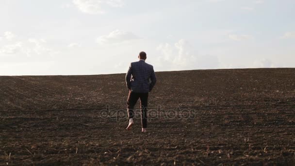 Uomo barbuto in giacca e cravatta sul campo a piedi nudi. Un bell'uomo barbuto sta camminando sul campo. Maschio in costume classico in natura . — Video Stock