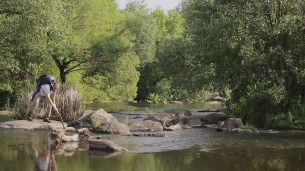 Homme barbu voyage le long du gué de la rivière. Un touriste avec un sac à dos traverse la rivière. Le barbu traverse la rivière . — Video