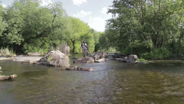 男は髭川フォードに沿って男旅です。バックパックと観光客は、川を横切る。ひげを生やした男が川を渡る. — ストック動画