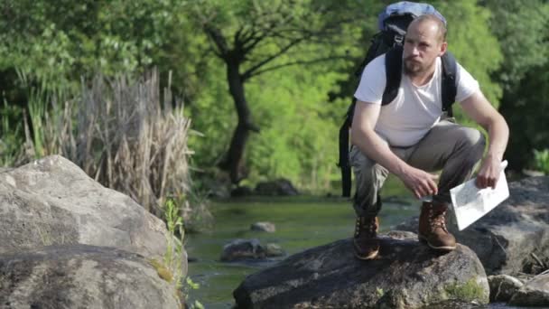 Guy bebaarde man reizen langs de rivier ford. Een toerist met een rugzak kruist de rivier. De bebaarde man kruist de rivier. — Stockvideo
