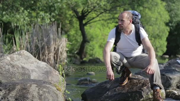 Guy bearded man travels along the river ford. A tourist with a backpack crosses the river. The bearded guy crosses the river. — Stock Video