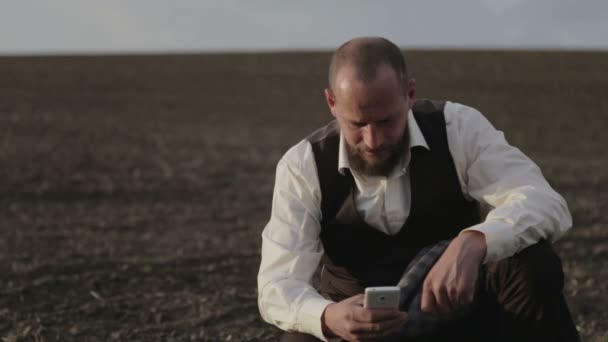 Een bebaarde landeigenaar gaat in het veld per telefoon. Een man in een pak spreekt emotioneel op de mobiele telefoon. Man met een baard in het veld met een telefoon. — Stockvideo