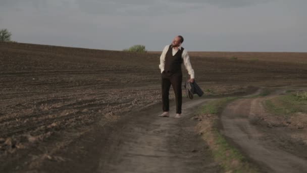 Hane i en klassisk kostym i naturen. En man i kostym är glad och dansar i fältet. — Stockvideo