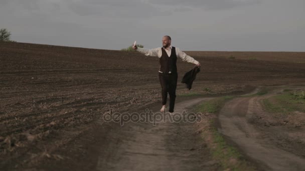 Hane i en klassisk kostym i naturen. En man i kostym är glad och dansar i fältet. — Stockvideo