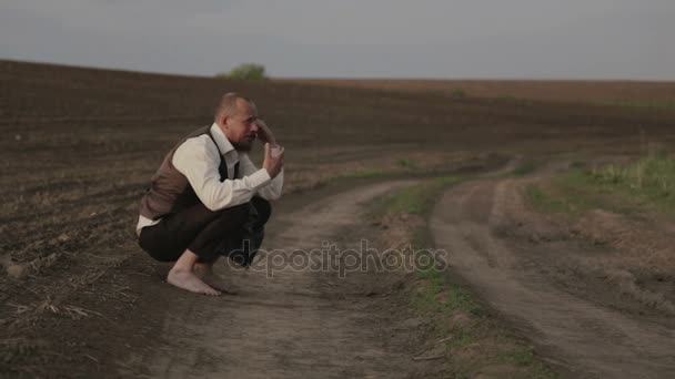 Brodaty właściciel ziemski w polu rozmawia przez telefon. Człowiek w garniturze emocjonalnie mówi na telefon komórkowy. Człowiek z brodą w polu z telefonem. — Wideo stockowe