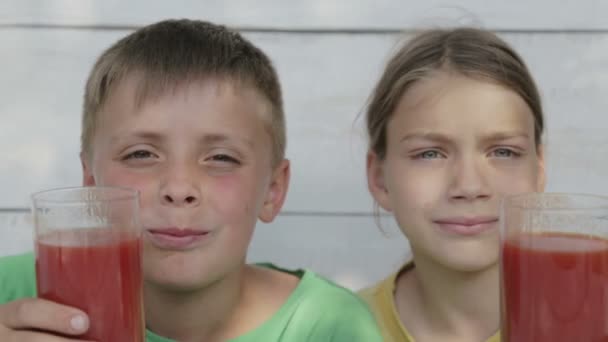 Kinderen op een witte achtergrond drinken tomatensap uit glazen. Twee jongens drinken tomatensap. Natuurlijke maaltijd, gezond voeden. — Stockvideo