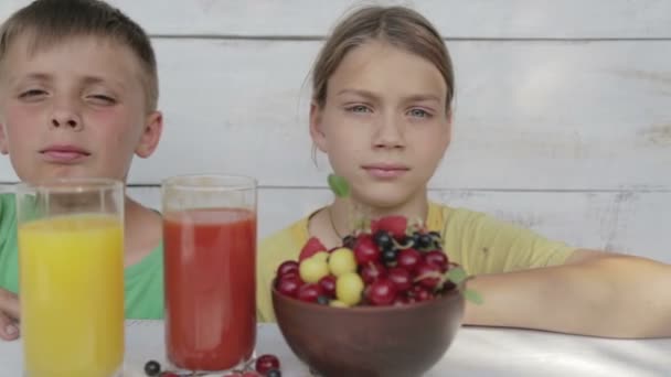 Los chicos beben jugo de naranja y tomate. Los niños beben jugo mirando en una cámara de cine . — Vídeo de stock