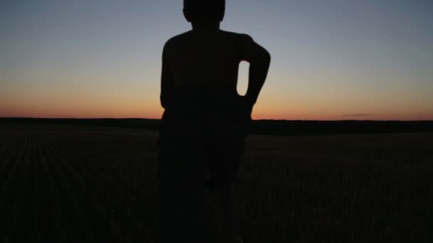 Il ragazzo al tramonto fa esercizi in giro per il campo. Il bambino al tramonto della giornata sul campo corre e fa esercizi . — Video Stock