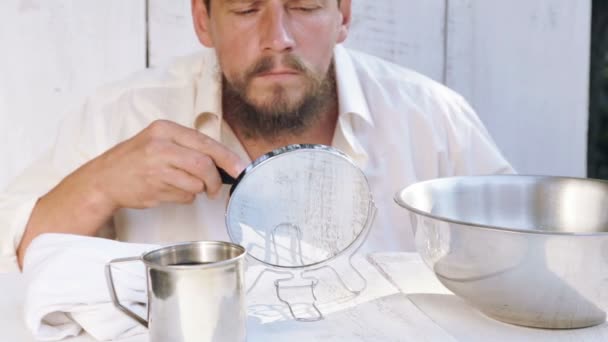 Un joven cuida su barba mientras está sentado en una mesa. Retrato de un hombre barbudo ocupado con su barba. Salud, higiene, belleza . — Vídeos de Stock