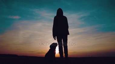 Bir kazak batımında köpek alanında önünde hood dansları ile bir adam. Bir genç ile bir köpek gün batımında rap dans silüeti.