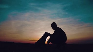 Bir çocuk ile bir köpek gün batımında portresi. Bir genç bir köpek ile bir alanda silüeti.