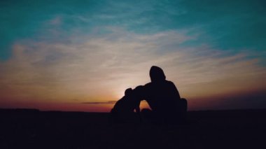 Bir çocuk ile bir köpek gün batımında portresi. Bir genç bir köpek ile bir alanda silüeti.