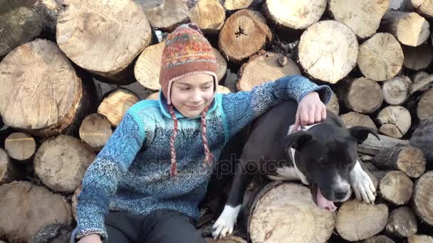Staffordshire terrier lambe um menino triste, no fundo de lenha. Retrato de uma criança no fundo de lenha com um cão vídeo 4K . — Vídeo de Stock