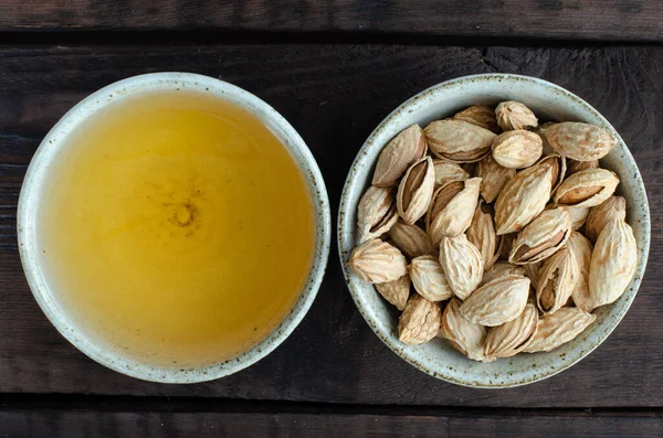 Green tea in cup and almonds in bowl on wooden background