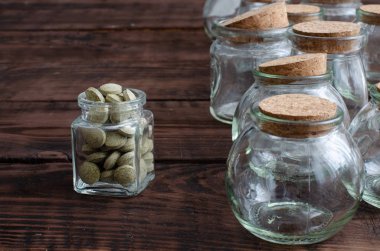 Bitkisel haplarla dolu küçük bir şişe ve tahta arka planda tıpası olan boş cam şişeler.