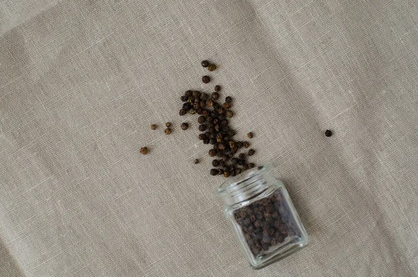 Black pepper from small glass bottle on linen background. Cloth background. Top view