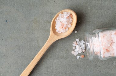 Himalaya kristal tuzu küçük cam şişeden ve pembe tuz tahta kaşıkta beton arka planda. Üst görünüm.