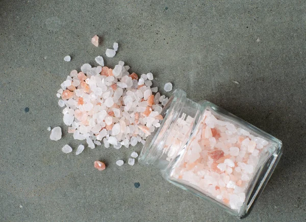 Himalayan crystal salt from small glass bottle on concrete background. Top view.