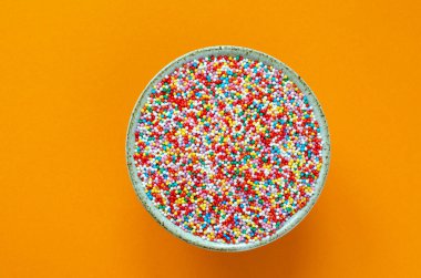 Turuncu arka planda kaseye renkli şeker serpiştirilmiş. Şekerleme serpintileri.