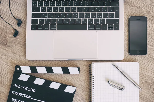 Film clapper laptop ve smartphone, ahşap sekmesinde kalem not defteri