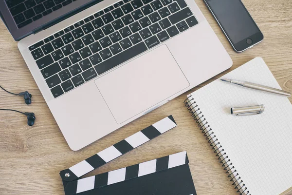 Film clapper laptop ve smartphone, ahşap sekmesinde kalem not defteri