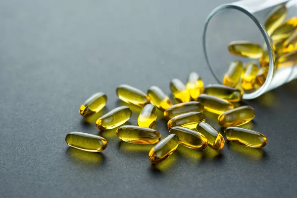 Fishoil capsules out of the small glass on black background — Stock Photo, Image